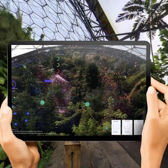 Hands holding a tablet up in the Rainforest and viewing an augmented reality overlay on the screen